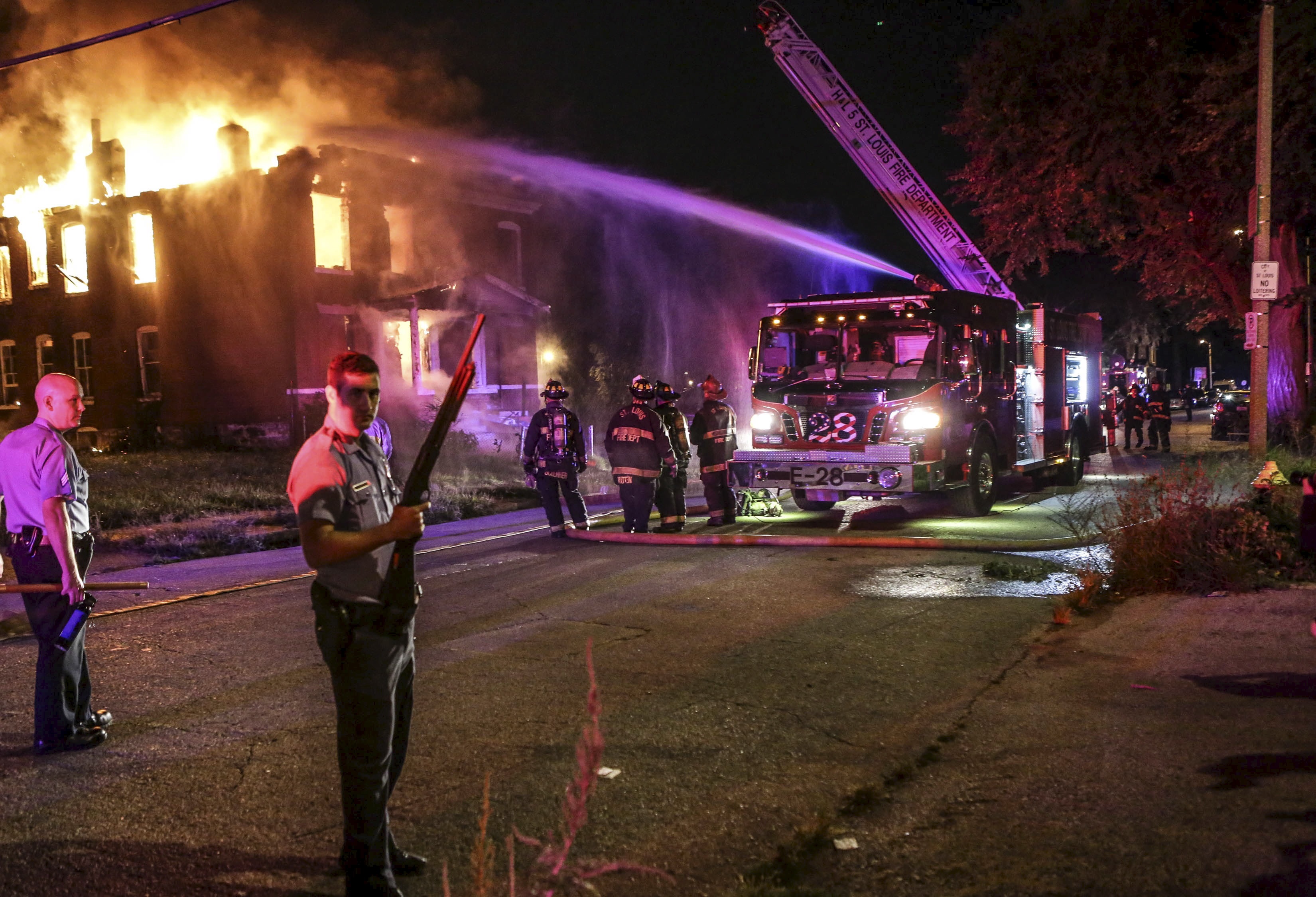 Firefighters attempt to put out a fire at an abandoned building with the protection of St. Louis City Police in St. Louis, Missouri August 19, 2015. According to eyewitness, protesters demonstrating against a police shooting earlier in the day in St. Louis set the building on fire. St. Louis police fatally shot a black teenager on Wednesday who they say pointed a gun at them, and later faced angry crowds, reigniting racial tensions first sparked by the killing of an unarmed black teen in another Missouri town a year ago. REUTERS/Lawrence Bryant TPX IMAGES OF THE DAY - RTX1OVQE