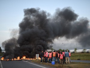 Workers on strike stand next to burning tyres as they block the access to the Total refinery of Donges, western france, on May 17, 2016 to protest against the government's planned labour law reforms. France's Socialist government has bypassed parliament and rammed through a labour reform bill that has sparked two months of massive street protests. / AFP PHOTO / JEAN-SEBASTIEN EVRARD