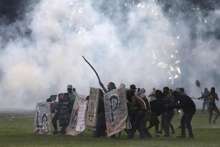 Protesters shield themselves as police fire tear gas at their demonstration outside Congress, where senators planned to vote on a spending cap bill and the lower Chamber of Deputies was considering controversial anti-corruption legislation, in Brasilia, Brazil, Tuesday, Nov. 29, 2016. Brazil, home to Latin America’s largest economy, is suffering its worst recession in decades. (AP Photo/Eraldo Peres)